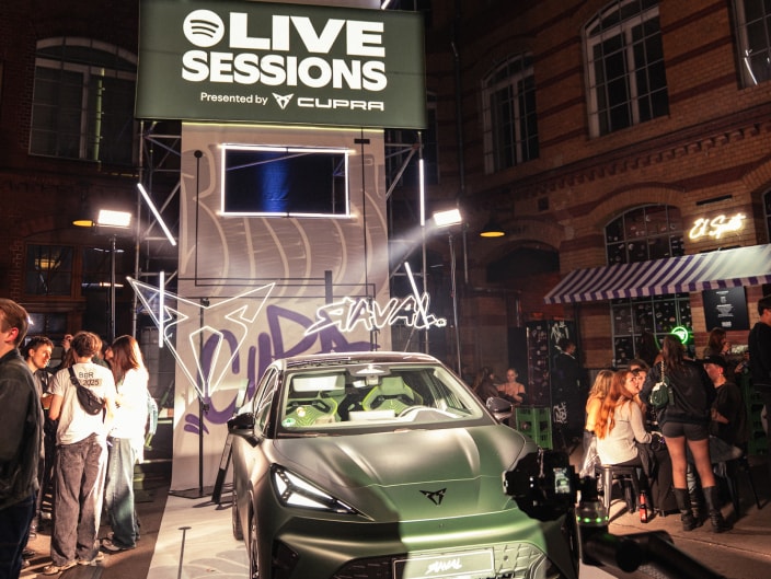 Mattgrüner CUPRA Raval vor der beleuchteten Event-Kulisse der Spotify Live Sessions mit Besuchern und Leuchtreklame bei Nacht.