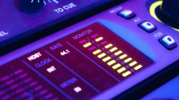 Nahaufnahme eines beleuchteten Mischpults und Ton-Equipment im Tonstudio.