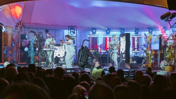 Musiker treten auf einer beleuchteten Festivalbühne vor Publikum auf.