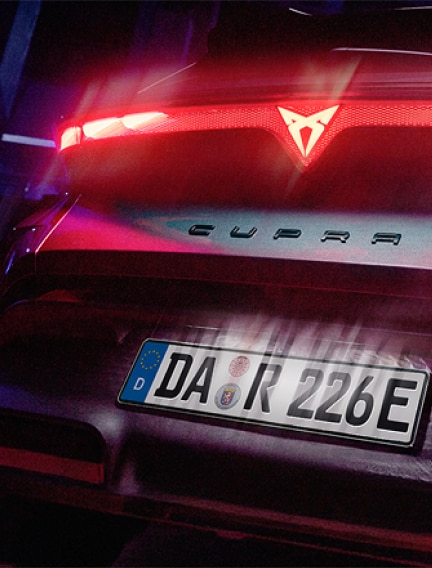 Heckansicht eines beleuchteten CUPRA Elektrofahrzeugs mit leuchtender Lichtleiste bei Nacht.