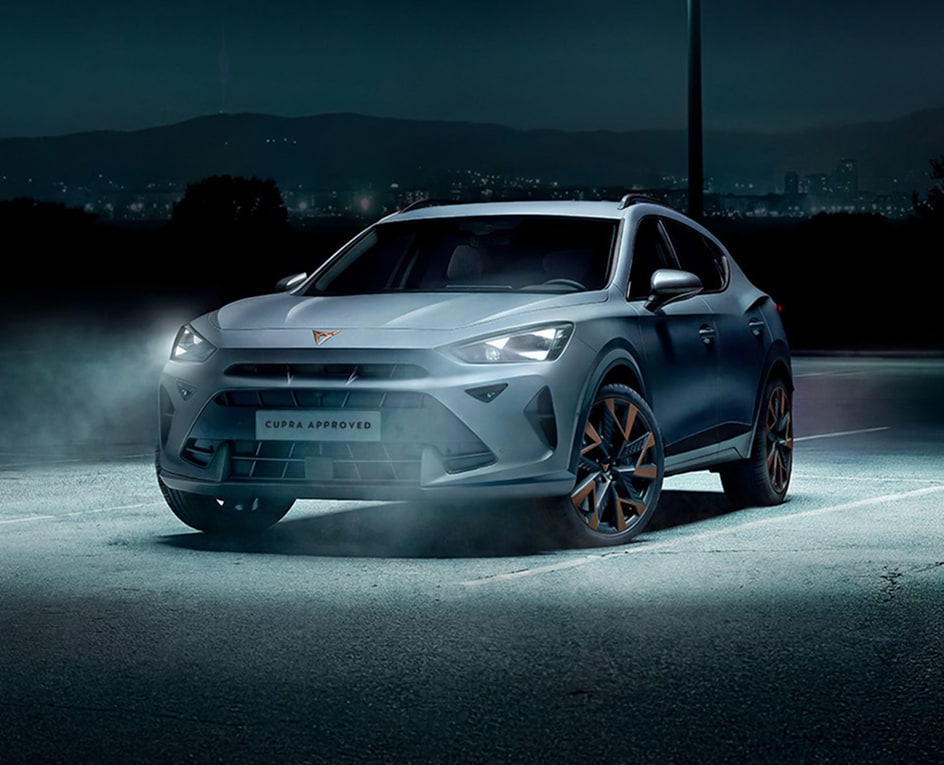Ein CUPRA Leon Sportstourer in mattem Grau steht seitlich vor einem modernen Industriegebäude. Rechts neben dem Fahrzeug steht ein Mann in dunkler Kleidung, der auf ein Tablet schaut.