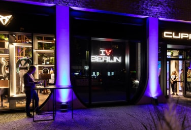 Außenansicht der CUPRA City Garage Berlin bei Nacht mit beleuchtetem ‚I CUPRA Berlin‘ Schriftzug und modernem Schaufenster.