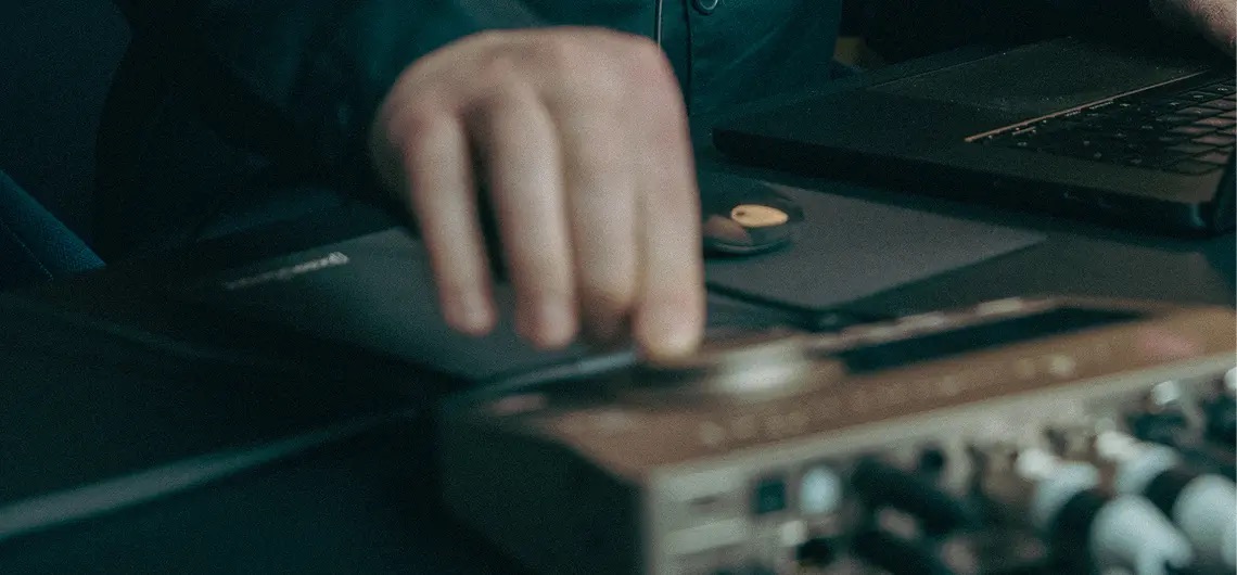 Nahaufnahme einer Hand an einem Audio Interface vor einem Laptop im Studio Setup.