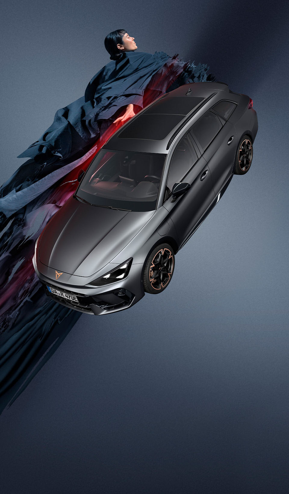 Ein CUPRA Leon Sportstourer, von oben gesehen, mit eingeschalteten Scheinwerfern, neben einer schwarzen Spinne, die von einem Felsvorsprung herunterhängt. Ein Ladekabel ist von einer Ladeeinheit an der Klippe mit dem Auto verbunden.