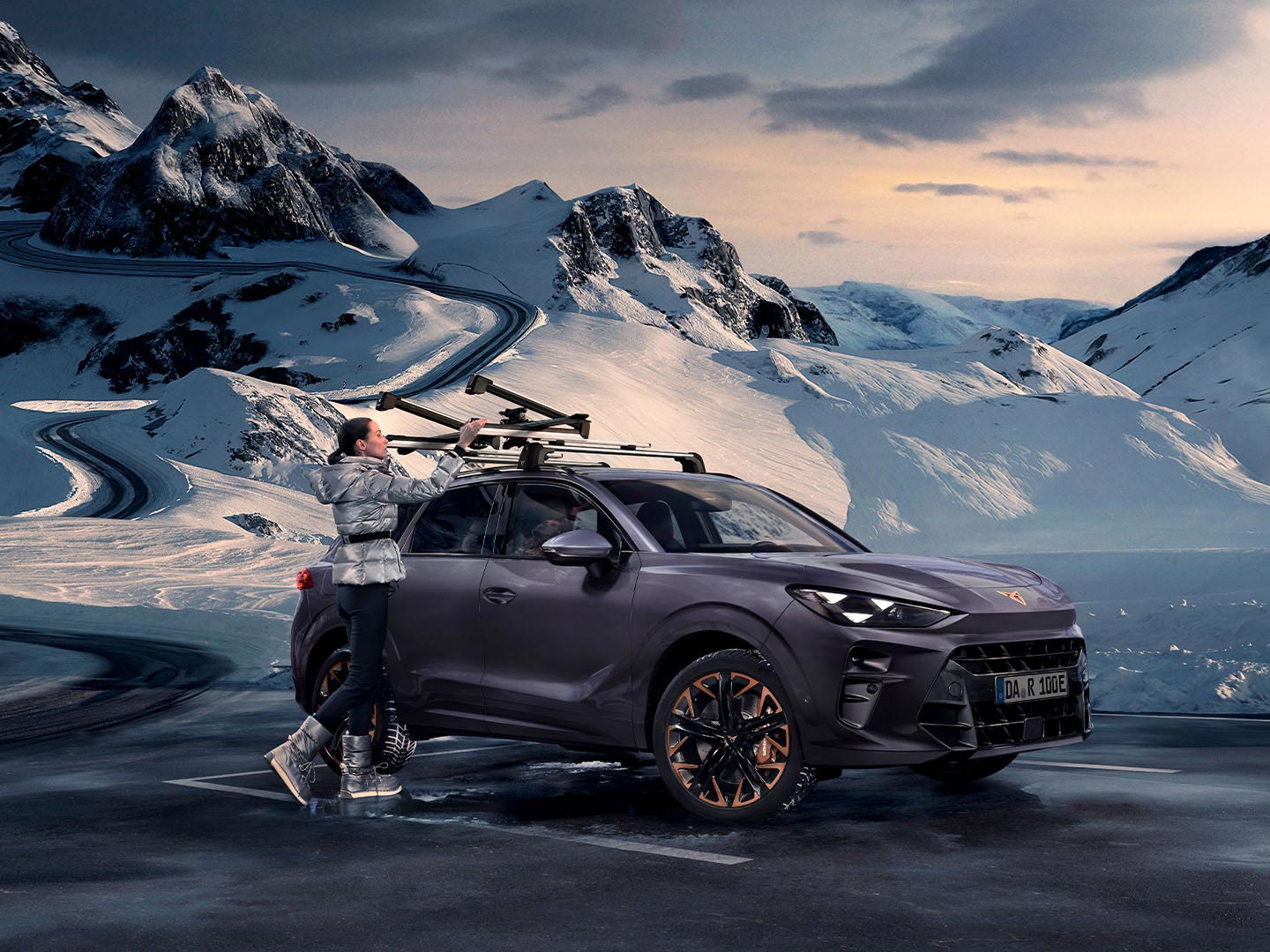 Ein CUPRA Terramar vor verschneiter Kulisse, auf dem der auf dem Dach montierte Skiträger – eines der Transportzubehörteile – zu sehen ist. Eine Frau nutzt diesen Träger, um ihre Skier zu transportieren.