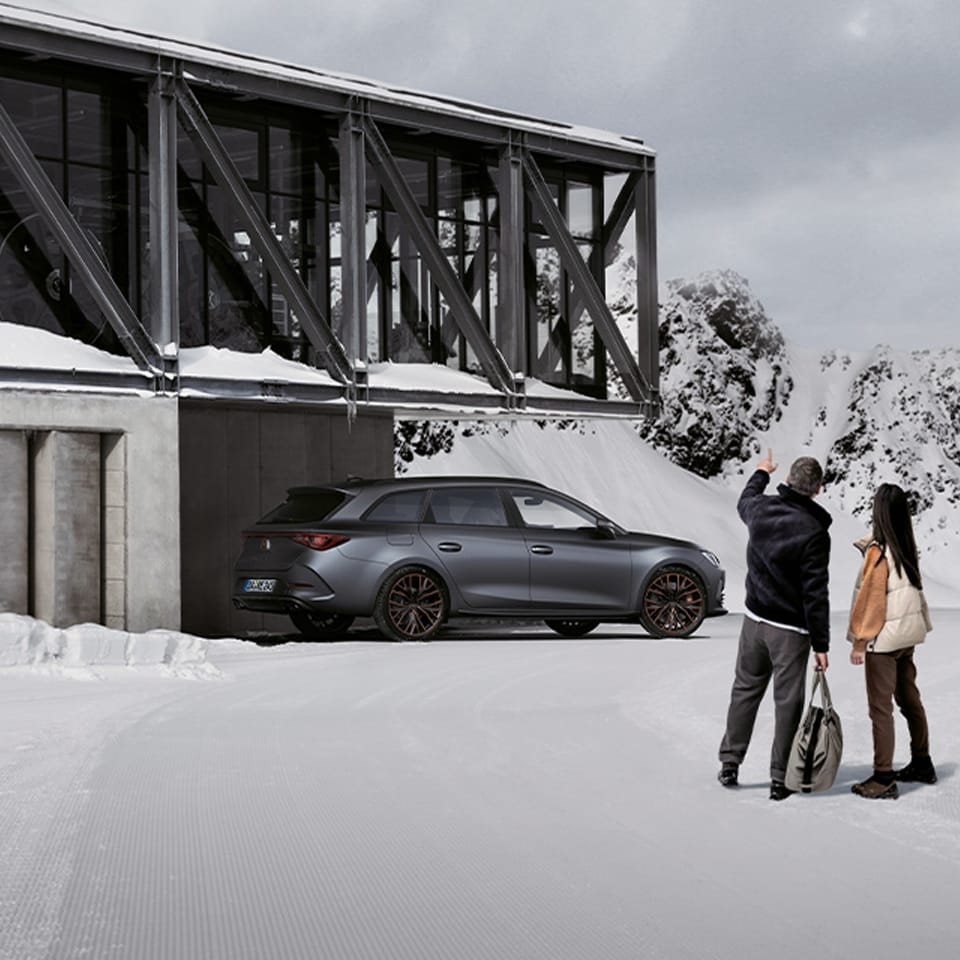 Seitenansicht des CUPRA Leon Sportstourer in einer verschneiten Landschaft vor einem modernen Gebäude.
