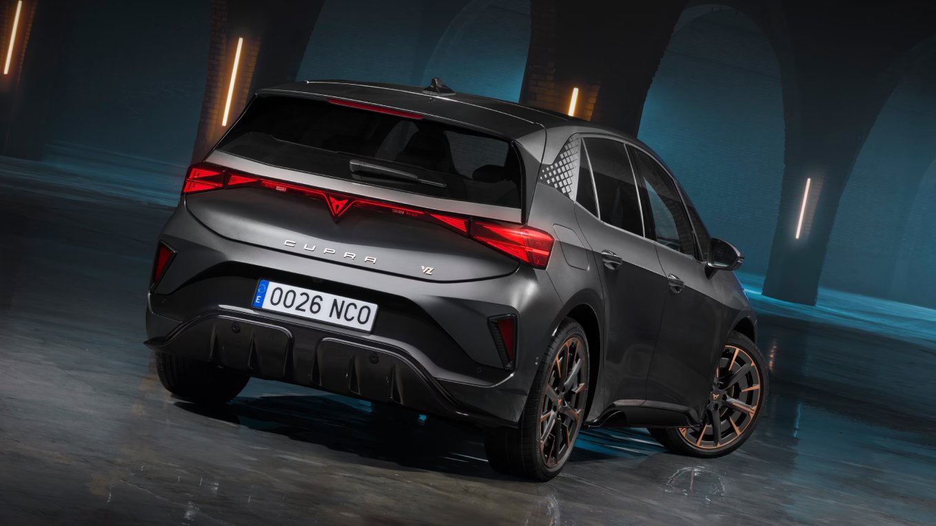 Vista traser de un CUPRA Born 2026 compacto deportivo 100% eléctrico en un entorno industrial amplio, iluminación tenue y pavimento húmedo