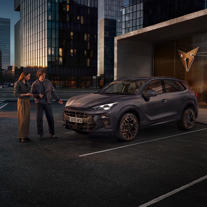 Dos personas junto a un CUPRA Terramar en color Dark Void aparcado frente a edificios al atardecer, observando el vehículo en un entorno urbano elegante.
