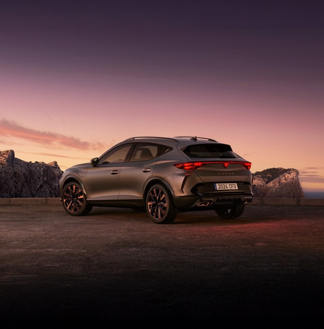 CUPRA Formentor e-HYBRID estacionado frente a una estructura arquitectónica moderna con reflejos en el suelo mojado.