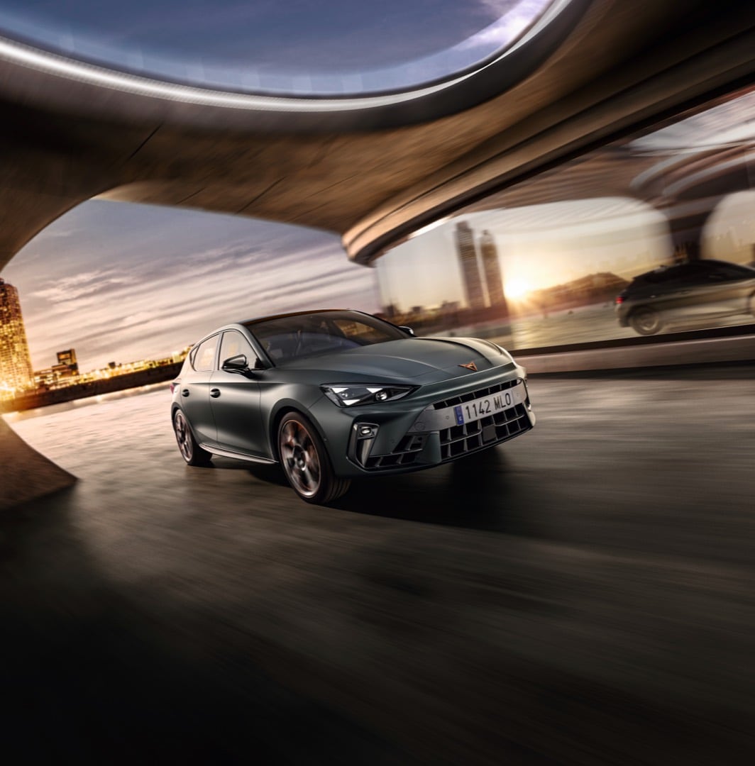 CUPRA León e-HYBRID 5 puertas color gris estacionado frente a una arquitectura contemporánea con iluminación dorada.