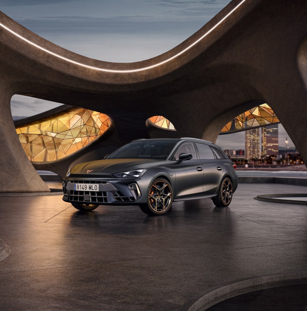 CUPRA León Sportstourer color gris oscuro estacionado al aire libre con paisaje urbano al fondo.
