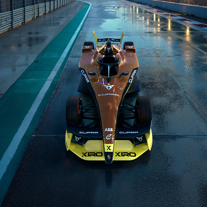 Vista frontal del CUPRA Kiro de Fórmula E, luciendo su librea inspirada en el diseño copper con audaces detalles en negro y amarillo, diseñado para la temporada 2025 de Fórmula E, sobre una pista de carreras mojada.