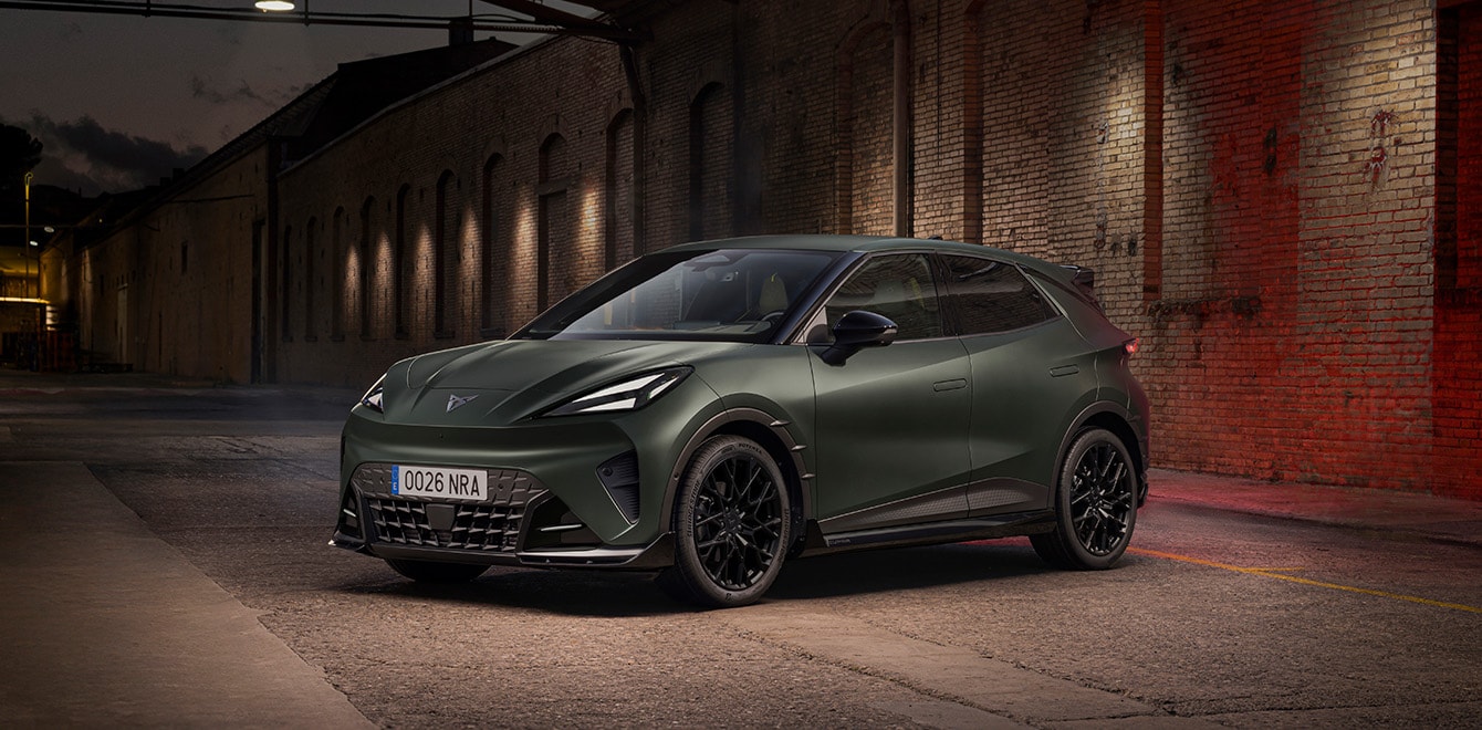 Une CUPRA Raval équipée du Custom Pack s'expose de trois-quarts face, révélant ses boucliers sportifs et sa calandre agressive devant de longs bâtiments industriels en briques éclairés.