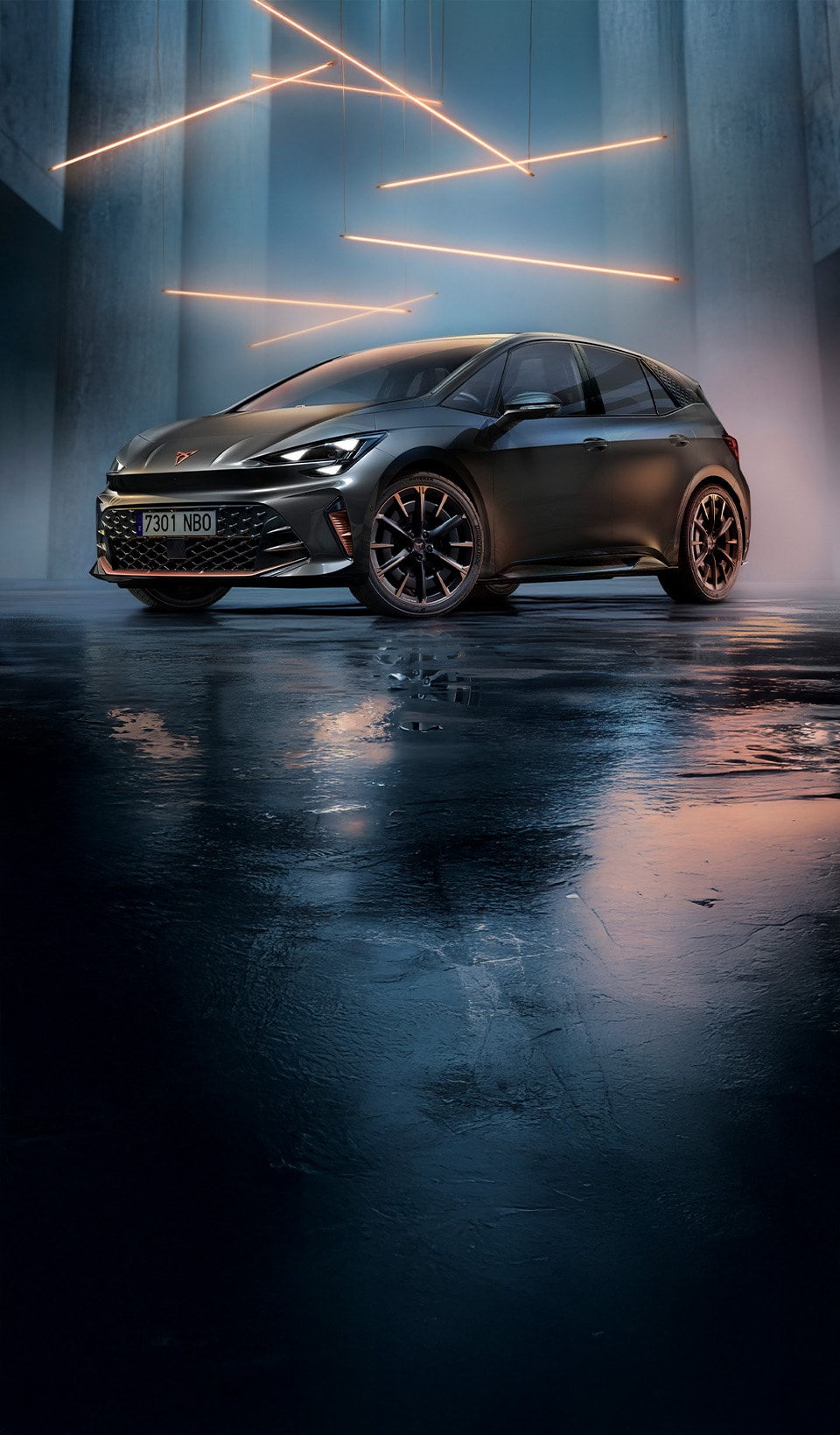Front three-quarter view of a CUPRA Born in Timanfaya Grey colour, parked in a minimalist concrete garage with a wet, reflective floor. The ceiling features horizontal linear metal lighting that illuminates the vehicle from above.