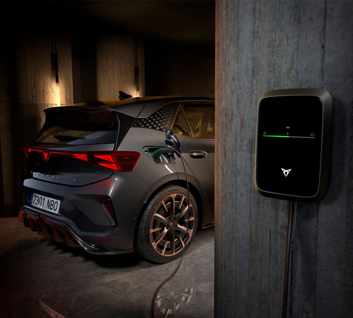 CUPRA Born VZ with copper alloy wheels charging from a wall-mounted home charger in a concrete garage.