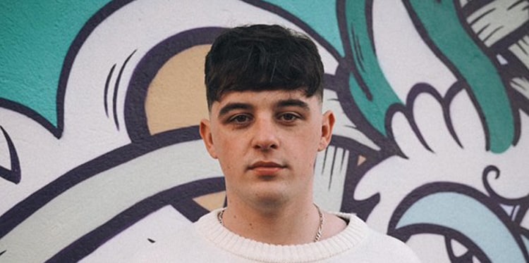 DJ BASIK, On The Pulse finalist, standing in front of a graffiti mural