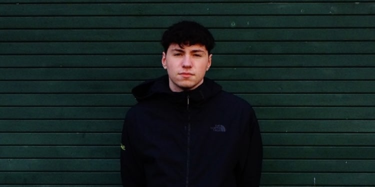 DJ Hallster, On The Pulse finalist, standing against a dark green metal shutter