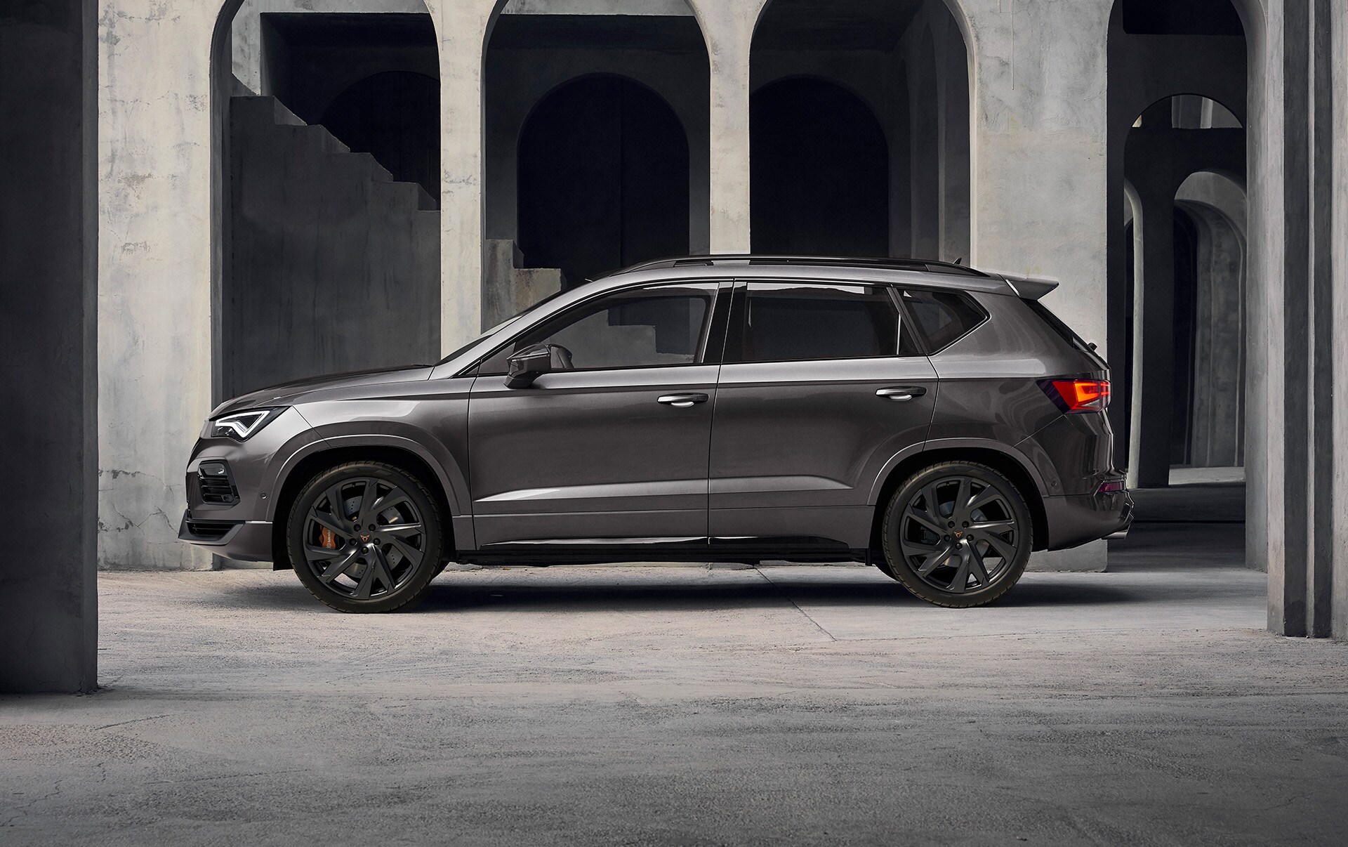 Boczna część CUPRY Ateca na tle betonowej budowli. Dobrze widoczne muskularne proporcje SUV-a. 