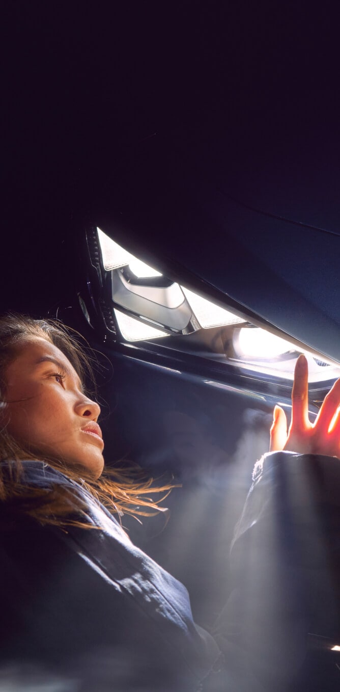 Close-up of a woman examining the CUPRA Tavascan's illuminated front logo at night.