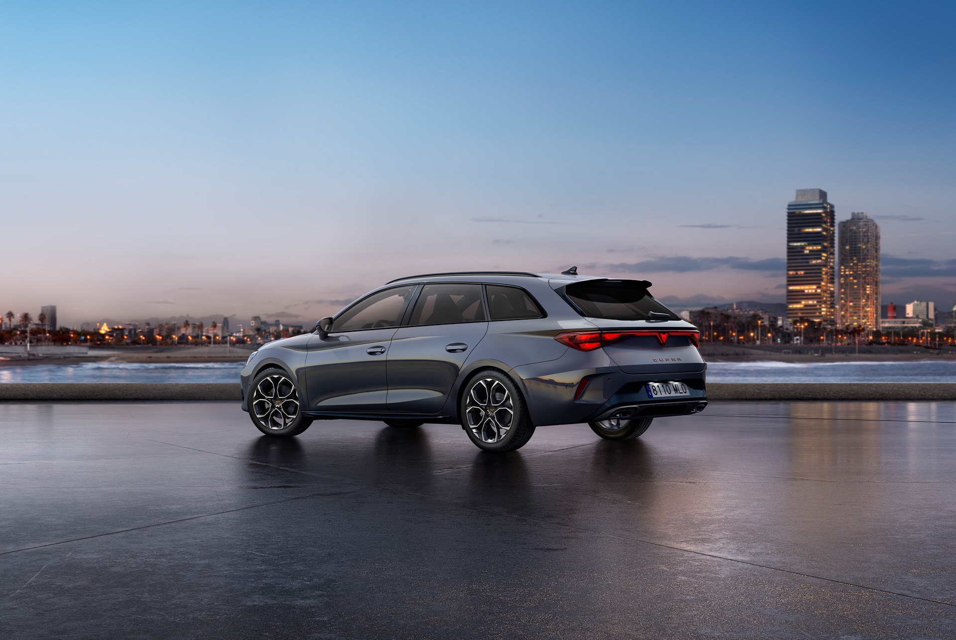 Rear view shot of Cupra Leon Sportstourer glossy grey car model with dynamic chassis control, plus black and copper alloy wheels. City in the background at sunset.