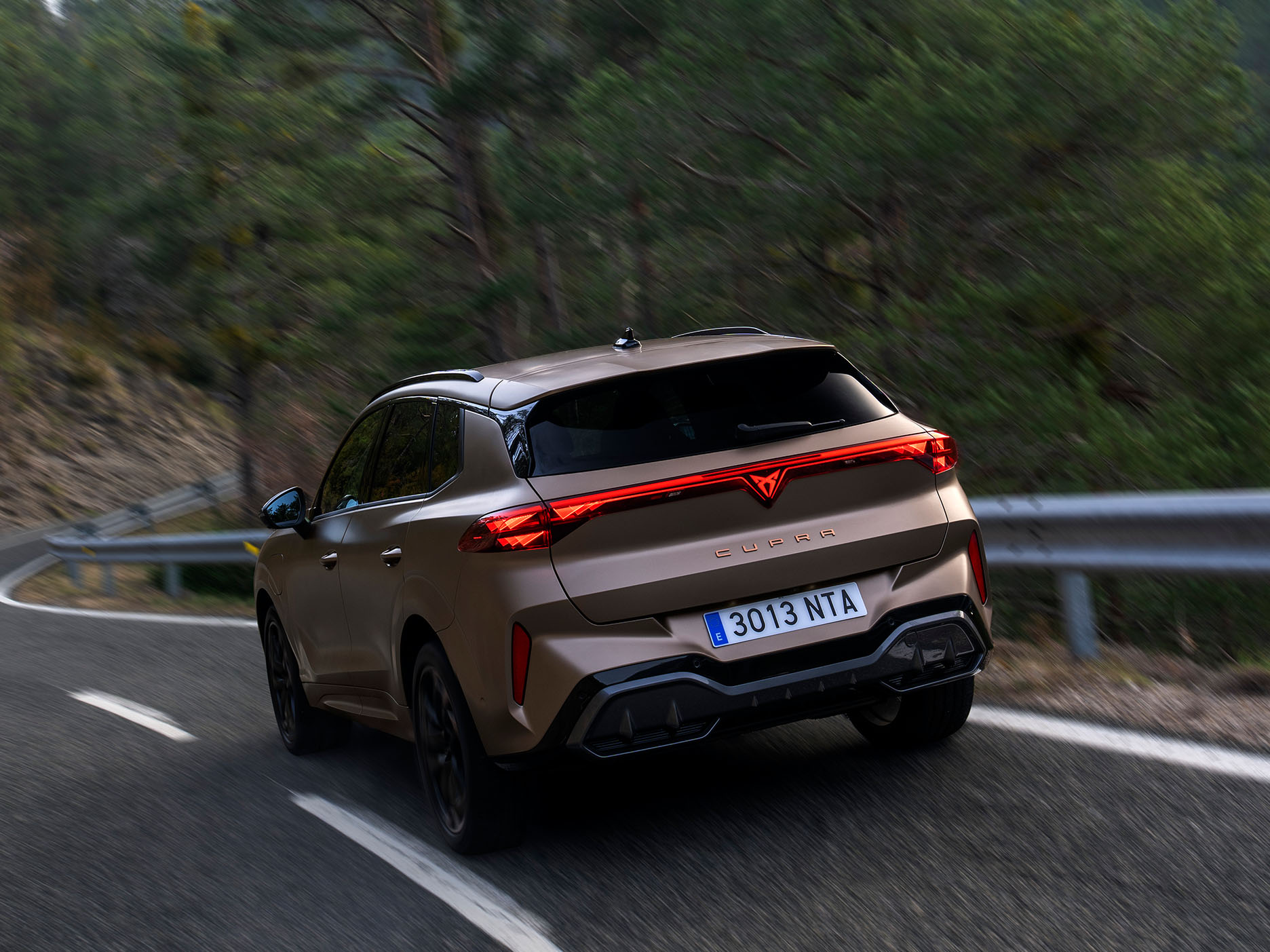 Vue du design arrière du CUPRA Terramar incluant les feux LED CUPRA, le logo 3D LED CUPRA et le nom du modèle Terramar. Le véhicule roule sur une route bordée d’arbres.