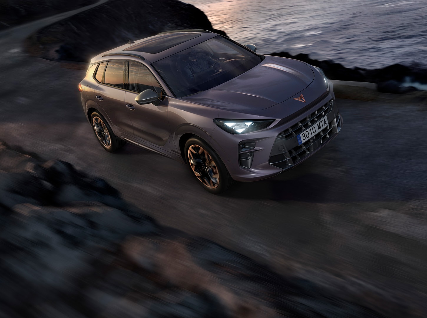 Cupra Terramar SUV in Timanfaya-Grau, Modelljahr 2025, mit 19-Zoll-Felgen in Cosmic Copper bei Sonnenuntergang am Meer. Hybrid-SUV zu verkaufen.
