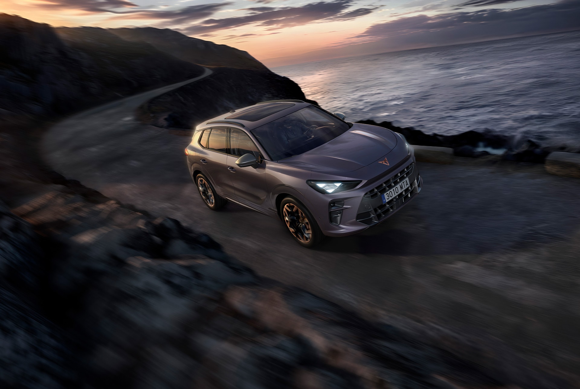 CUPRA Terramar 2025, the best compact sport utility car, driving along a coastal road featuring dark void paint, 20” hadron copper alloys and high canyon leather seats.