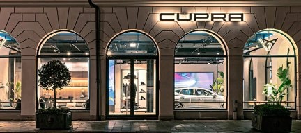 Elegant exterior of a CUPRA City Garage at night, where a classic stone façade and arched windows frame a glowing CUPRA emblem.