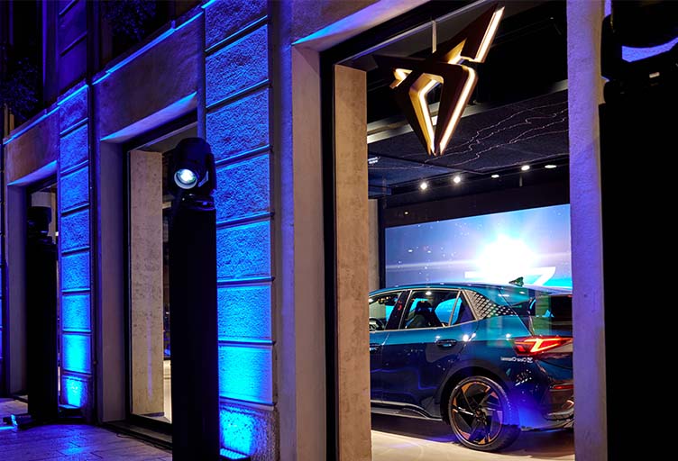 Blick in die CUPRA City Garage Mailand mit blauem CUPRA Born im Showroom und beleuchtetem CUPRA Logo.
