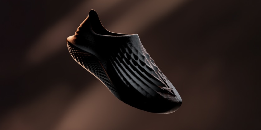 Single, dark, futuristic-looking slip-on shoe floats in a dimly lit space with a unique design.