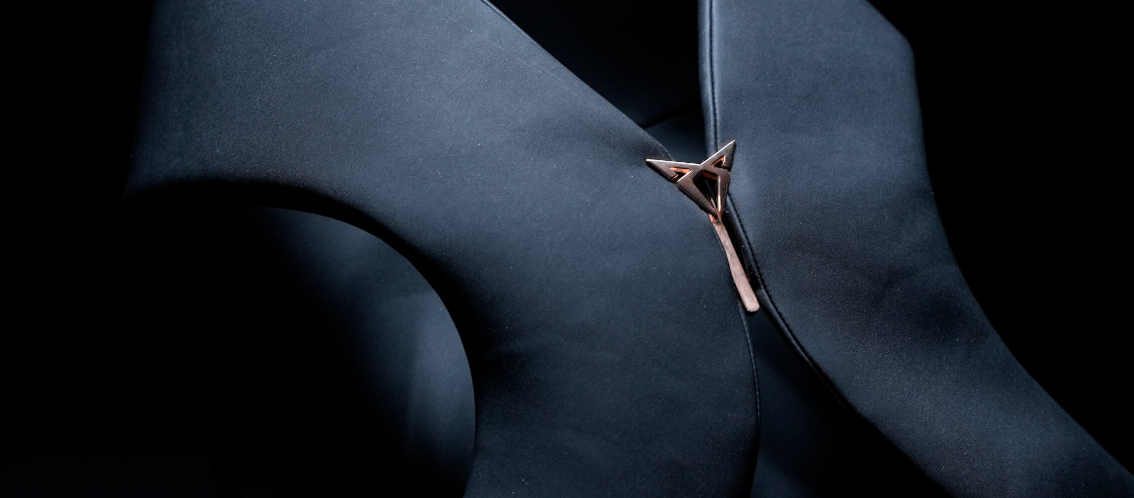 A close-up shot of dark fabric garment with a unique metal fastener, against a dark background.