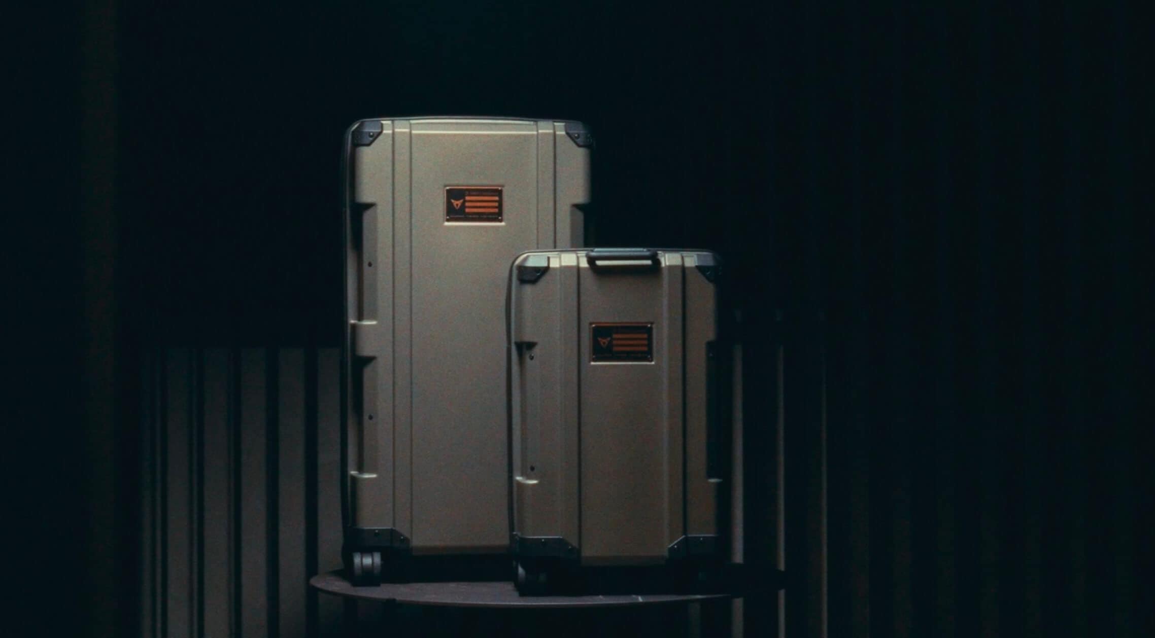 Two hard-shell suitcases of varying sizes are displayed in a room with a black background.
