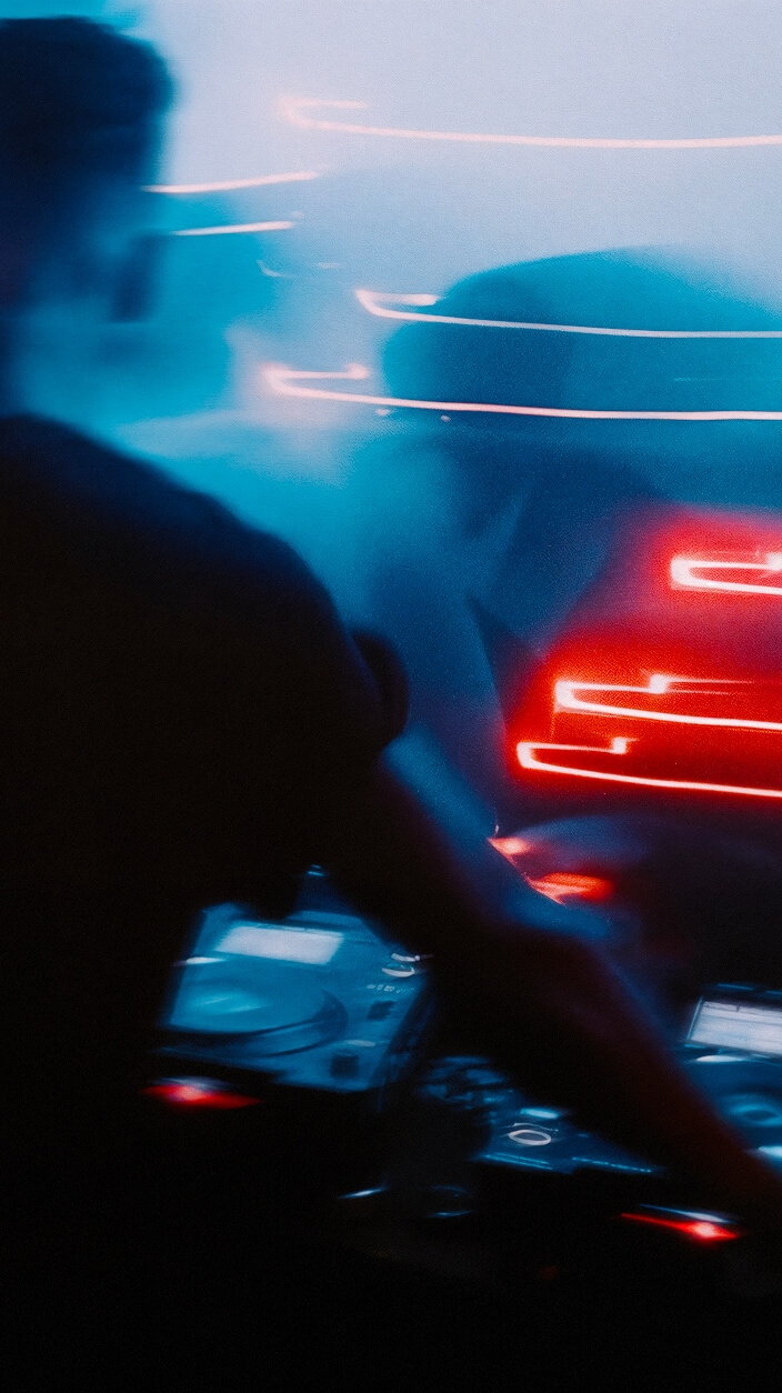 A blurred image of a DJ with equipment, surrounded by vibrant streaks of red and blue lights, with a music event in the foreground.