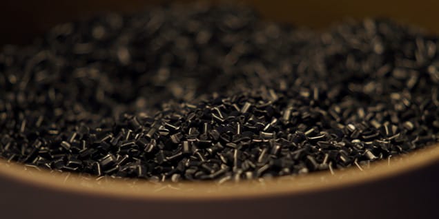 The image shows a close-up view of small black plastic pellets or granules, commonly used as raw material in plastic manufacturing and injection molding processes.