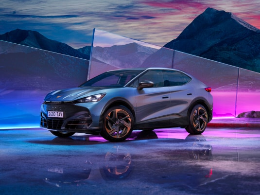 Cupra tavascan electric car offer, suv coupe in tavascan blue colour with 21 inch katla wheels. Glass panel and sky background.