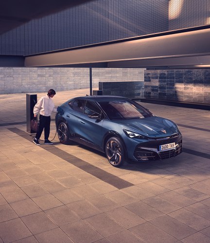 electric car cupra leon charging in car park with wall charger, ambient lighting, concrete and sky