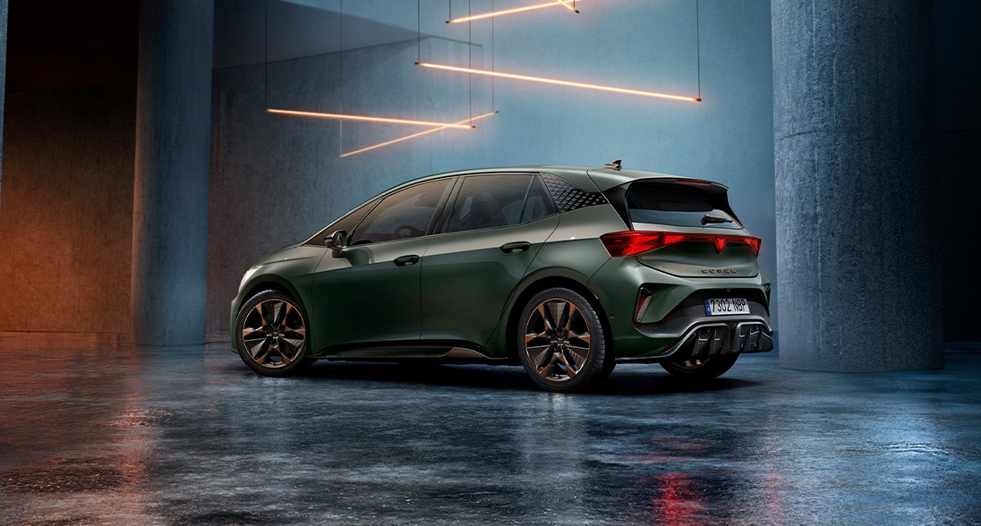 A dark green Cupra Born electric hatchback parked in a minimalist, concrete-walled space, viewed from the rear three-quarter angle.