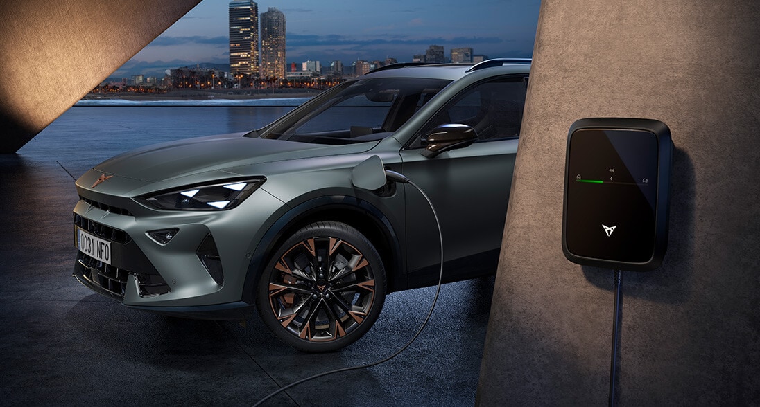 Enceladus grey matt electric cupra formentor suv plugged into an EV charging wallbox with a city skyline in the background.