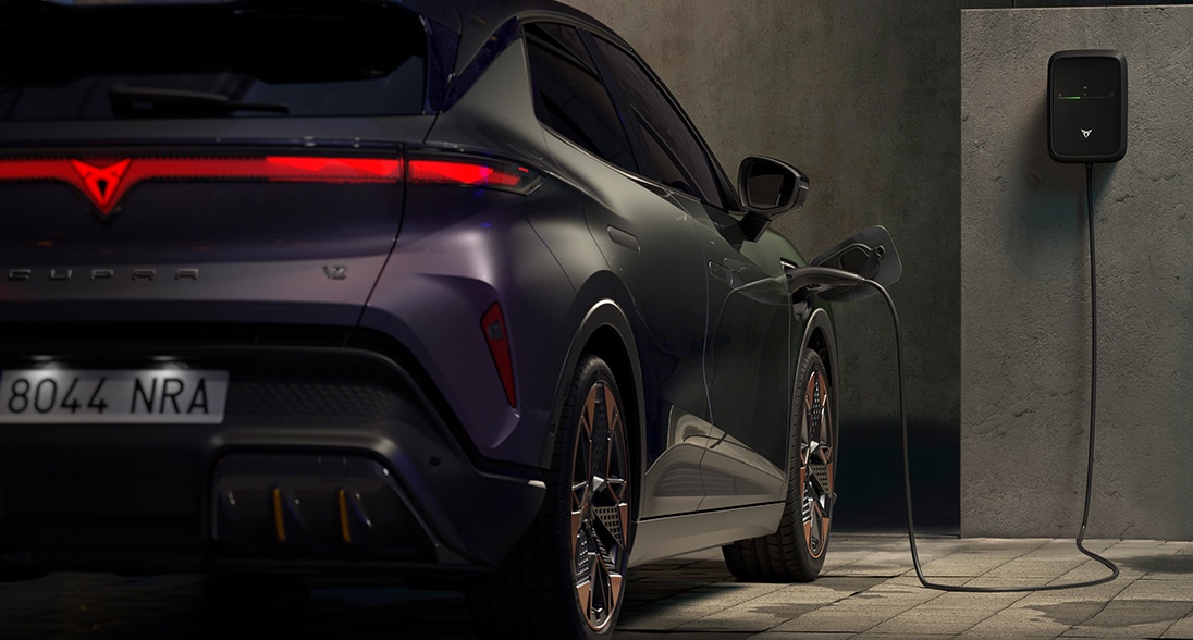Rear view of a cupra tavascan electric SUV parked on a reflective surface with mountains and a colourful sunset sky in the background.