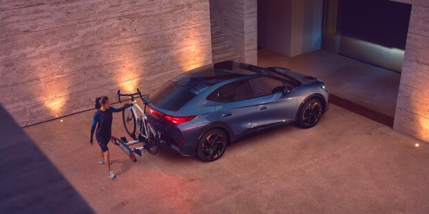 A person loading a bike onto a cupra tavascan parked in a modern driveway, showing the EV’s versatility for active lifestyles.