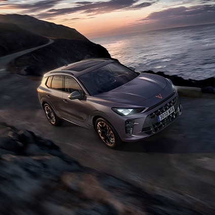 A CUPRA SUV driving on a coastal road during sunrise, representing the brand's vision. 