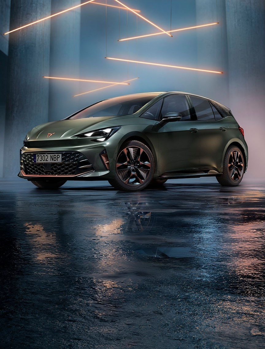 Front three-quarter view of a CUPRA Born in Dark Forest colour, parked in a minimalist concrete garage with a wet, reflective floor. The ceiling features horizontal linear metal lighting that illuminates the vehicle from above.