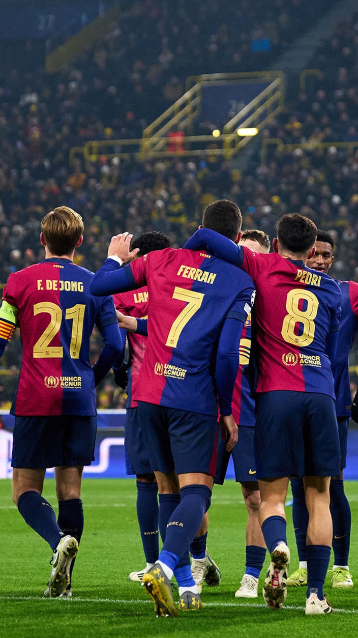 FC Barcelona football players seen from behind celebrating on the pitch during a match. Players wearing the iconic blue and red jerseys, including Frenkie de Jong (21), Ferran (7), and Pedri (8), huddle together in front of a packed stadium crowd.