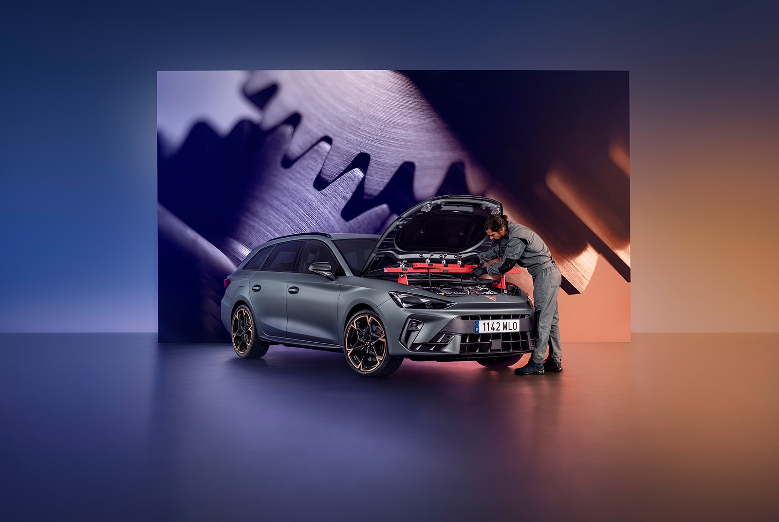 A car technician in a grey jumpsuit leans into the open, red-lit engine bay of a CUPRA car. The scene is set in a modern service area with a large background graphic of interlocking mechanical gears.
