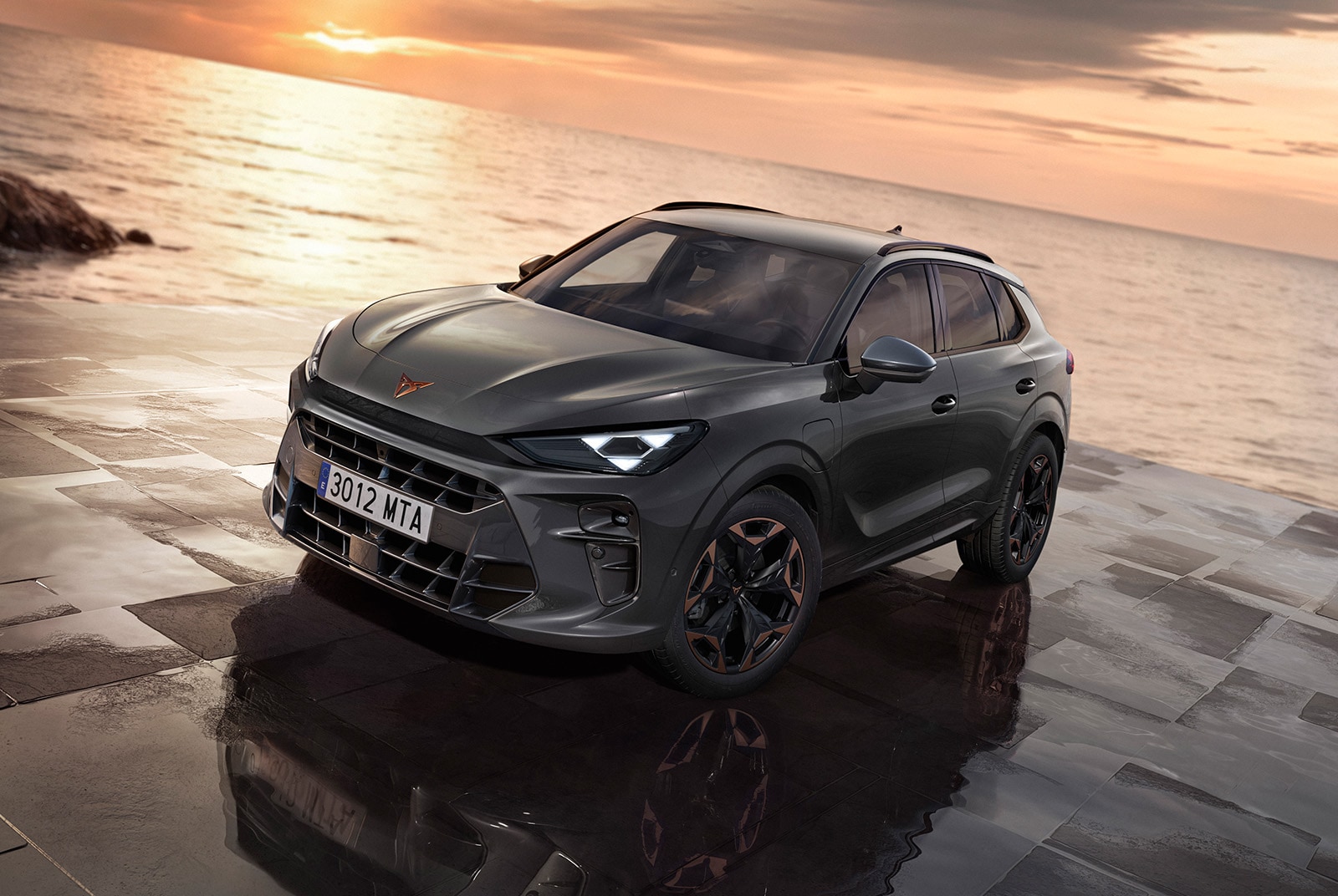 A CUPRA Terramar parked on a wet, reflective stone pavement next to the sea at sunset. The vehicle features illuminated geometric headlights and black wheels with copper accents. 