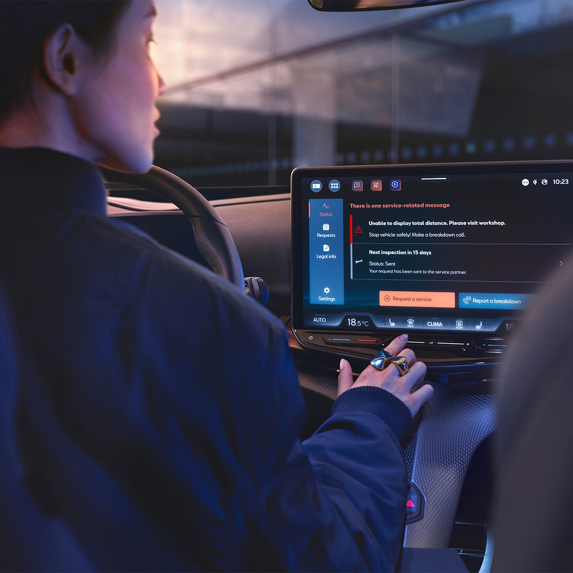 An over-the-shoulder view of a woman in the driver's seat of a CUPRA car, interacting with a large central touchscreen display that shows vehicle service notifications and maintenance options.