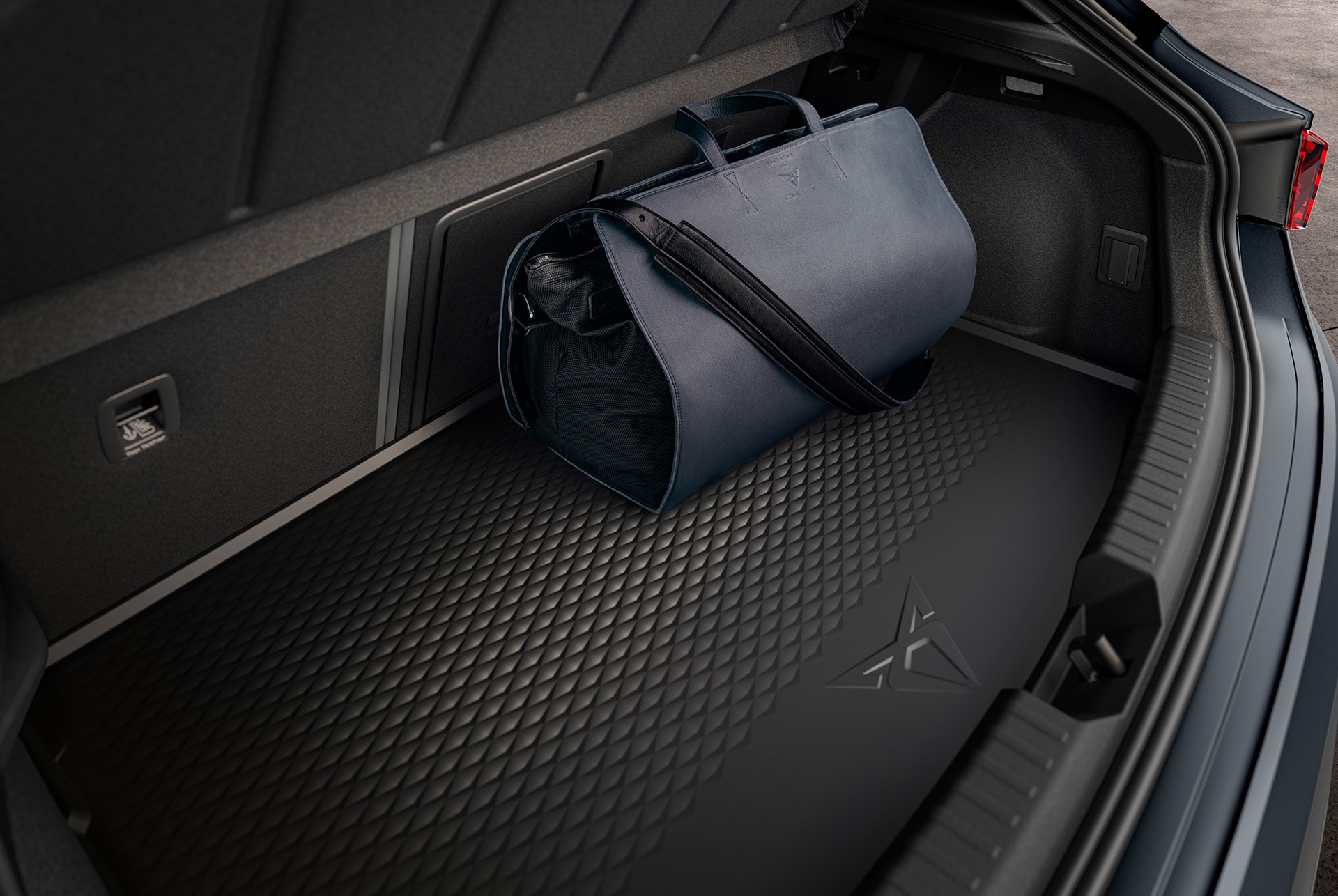 A close-up view of a CUPRA Leon's trunk, featuring a fitted, textured black rubber boot liner with the CUPRA logo. A dark blue duffel bag sits on the left side of the liner.