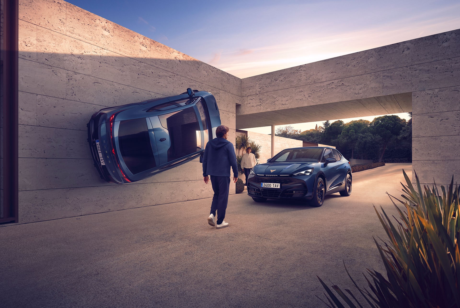 In the courtyard of a modern concrete building at sunset, a blue CUPRA is mounted vertically on a large wall like a piece of art. Below, a person walks toward an identical blue CUPRA parked on the ground.