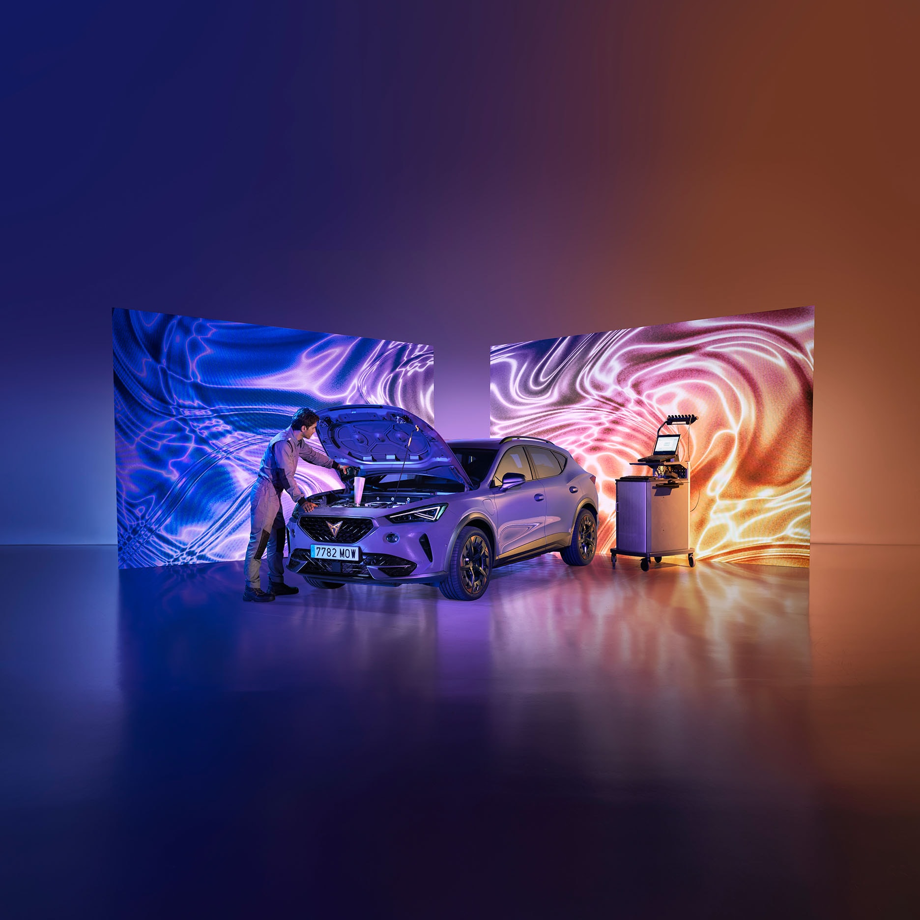 A car technician in overalls works on the open engine of a CUPRA car in a high-tech service area. A diagnostic computer on a cart stands nearby, and the background features large screens showing flowing, abstract patterns of blue and orange light on a reflective floor.