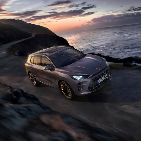 Front view of a cupra terramar, driving, on a road in the dark next to the sea.